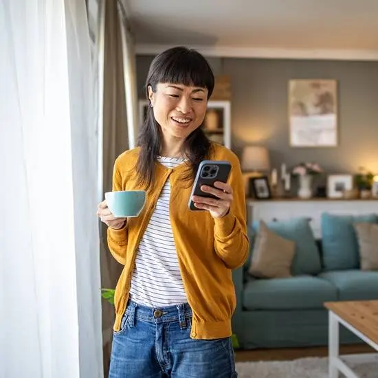 Woman smiling looking at her phone and holding a coffee cup