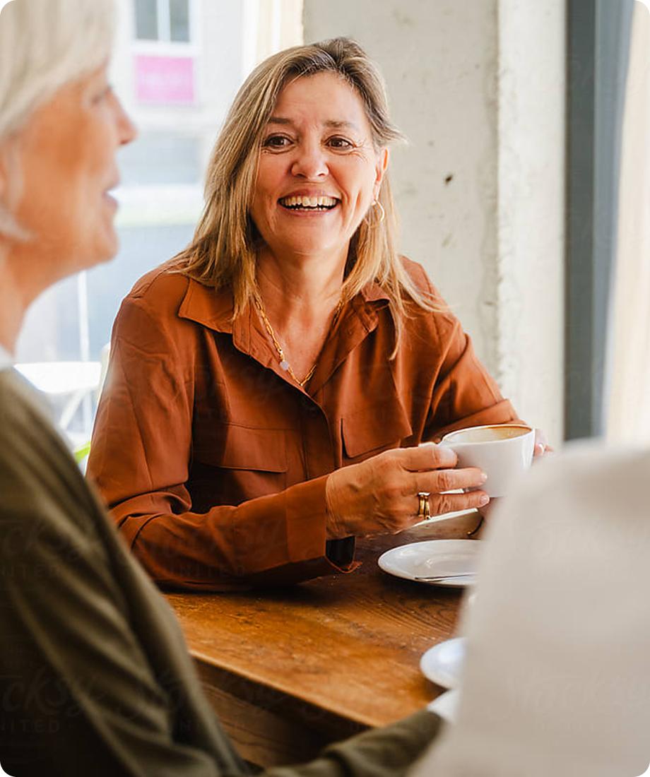 woman holding a coffee cup sitting at a table and smiling at the woman across from her