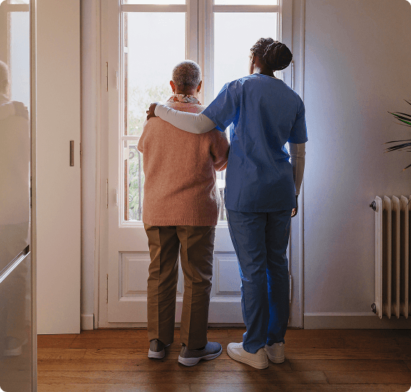 nurse standing and looking out the window with arm around patient