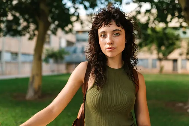 young woman with curly hair looking into camera with neutral expression
