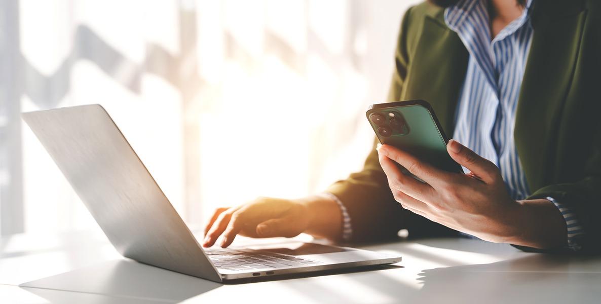 person holding a smartphone and typing on a laptop